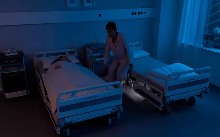 Patientenzimmer in der Nacht. Eine Patient steht auf und verlässt das Bett. Das Assistenzsystem reagiert und sendet ein Signal.