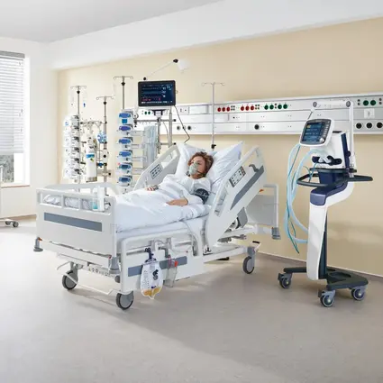 Chambre d’hôpital avec le lit Evario-one et l’équipement médical, équipé de long-pans à glissière et de rails normalisés pour des soins optimaux du patient.