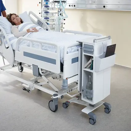 Członek personelu dekontaminacyjnego wypycha łóżko z pokoju, a szafka przyłóżkowa Quado jest wygodnie przymocowana do łóżka.