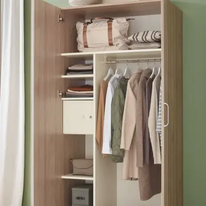 Geöffneter Holzkleiderschrank mit Kleidung, Schuhen und Stauraum vor grüner Wand