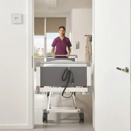 Pflegekraft schiebt schmales Evario one Bett mit 89 cm Breite durch Tür