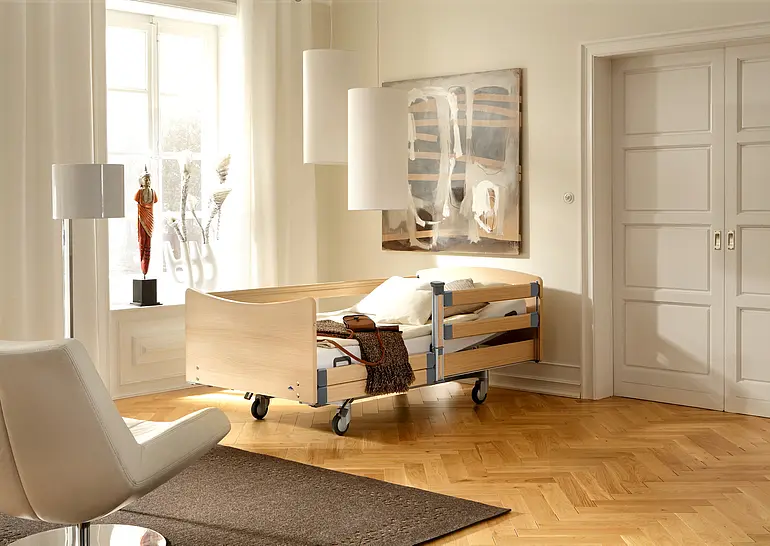 Elvido forto Schwerlastbett mit Holzdekor und integrierter Seitensicherung für sichere Mobilisation im Pflegezimmer.