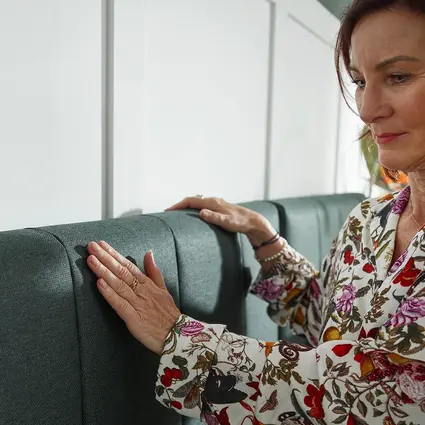 De vrouw streelt met haar hand het gestoffeerde hoofdeinde van het Libra - variant deluxe lifestylebed.