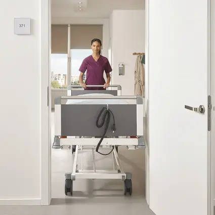 El cuidador empuja la estrecha cama Evario one de 89 cm de ancho a través de la puerta