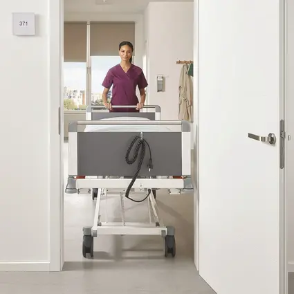 Le personnel soignant pousse un lit Evario étroit d’une largeur de 89 cm à travers une porte