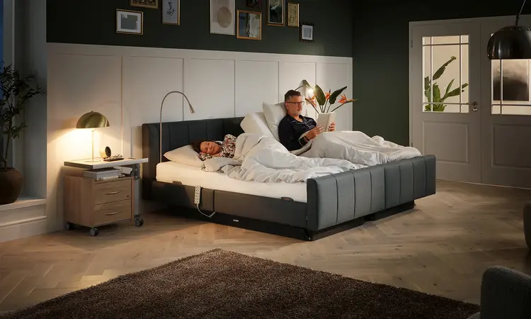 Une femme âgée lit dans le lit confort Libra deluxe de Stiegelmeyer dans un environnement moderne.