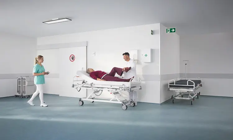 Lit hospitalier Evario one présenté sans système de protection latérale pour un accès sans entrave au patient et des soins flexibles.