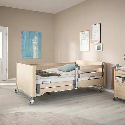 Lit de soins pour charge lourde Arena avec système de protection latérale en aspect bois chêne Lindberg et roulettes pour une mobilisation en toute sécurité.