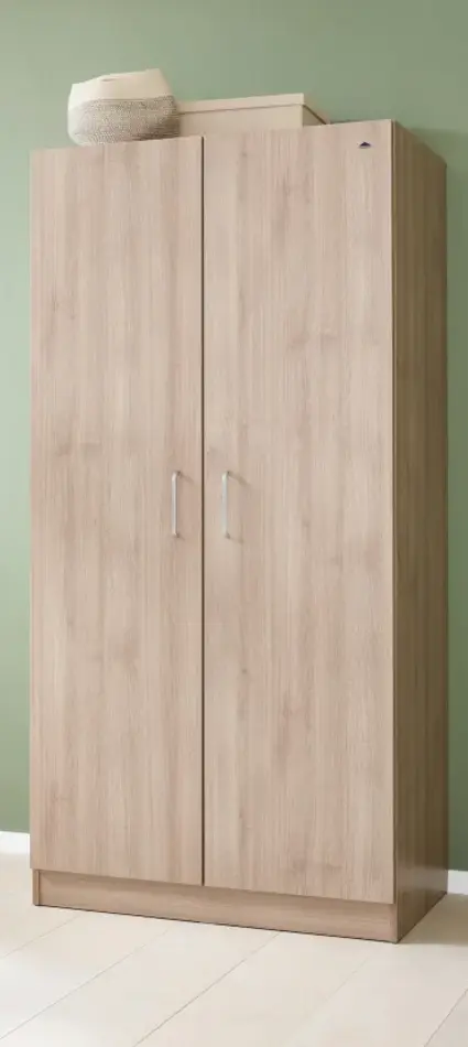 Geschlossener Holzkleiderschrank vor grüner Wand mit Dekoboxen auf dem Schrank