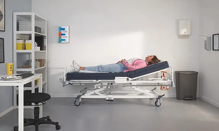 Nowoczesne łóżko szpitalne Evario one w ambulatoryjnej sali zabiegowej w centrum medycznym.