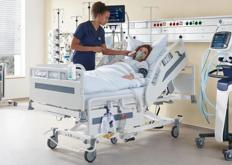 Dans une chambre d’hôpital équipée d’un lit et de matériel médical, une infirmière prend la température d’une patiente.