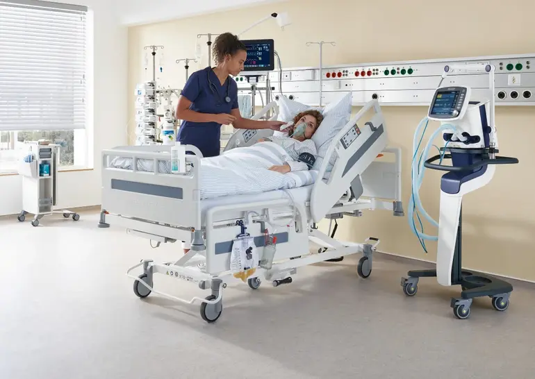 Dans une chambre d’hôpital équipée d’un lit et de matériel médical, une infirmière prend la température d’une patiente.