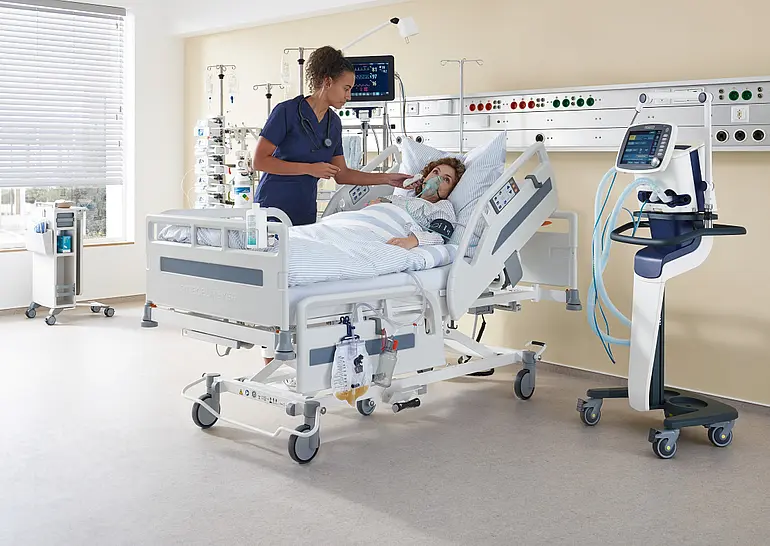 Dans une chambre d’hôpital équipée d’un lit et de matériel médical, une infirmière prend la température d’une patiente.