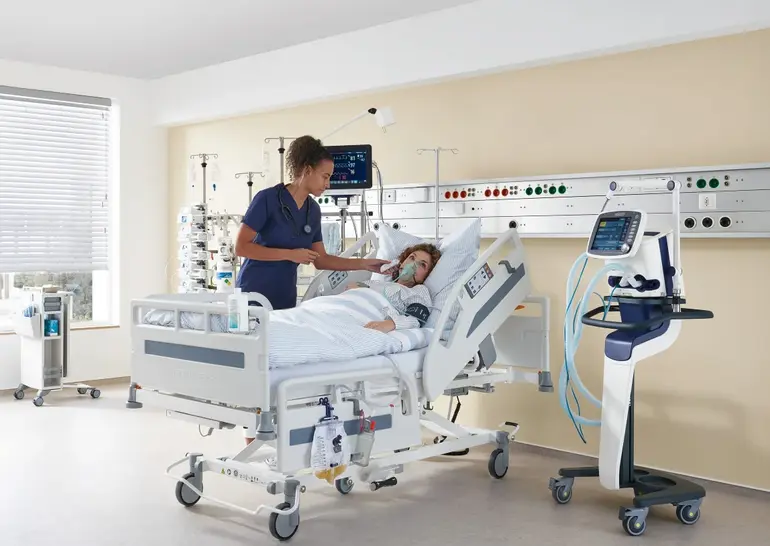 Dans une chambre d’hôpital équipée d’un lit et de matériel médical, une infirmière prend la température d’une patiente.