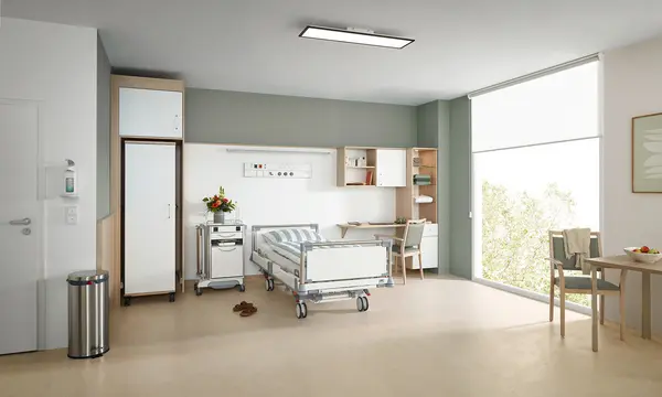 Puro ziekenhuisbed van Stiegelmeyer in een moderne optionele servicekamer met nachtkastje, kledingkast, bureau en zithoek bij het raam