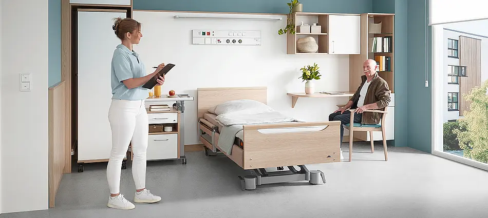 Elvido Pflegebett kombiniert mit maßgeschneiderten Objektmöbeln und Schränken im Bewohnerzimmer.