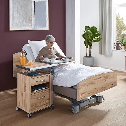 Elvido vervo Pflegebett mit verstellbarer Rückenlehne und Nachttisch Aparto für komfortable Mahlzeiten im Pflegezimmer.