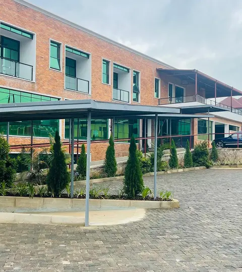The entrance to the Solace Clinic in the Rwandan town of Kabuga is located on a paved square. The modern hospital has a red brick front and green window glass.