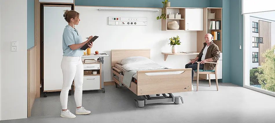 Cama de cuidados Elvido combinada con mobiliario a medida y armarios en habitación de residente.