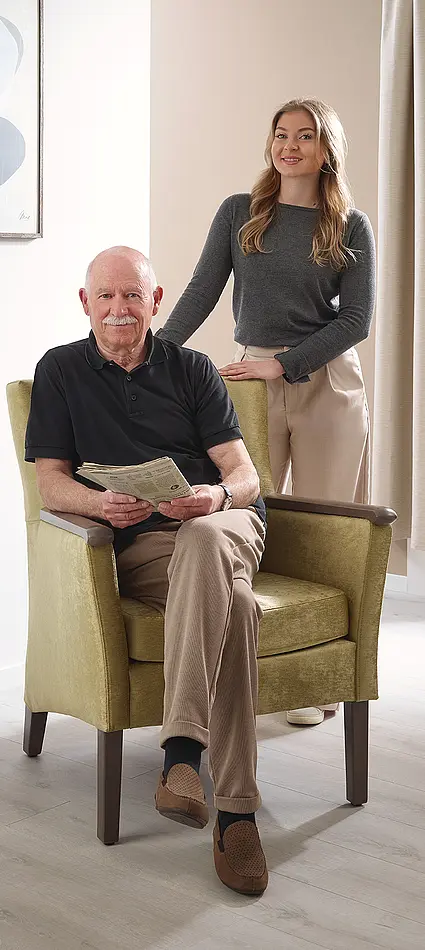 Un anciano está sentado en el sillón Luna y una joven permanece de pie junto a él en la habitación de cuidados