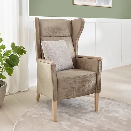 Cadeira de apoio Luna com encosto alto, pés de madeira e almofadas em um quarto de cuidados moderno.