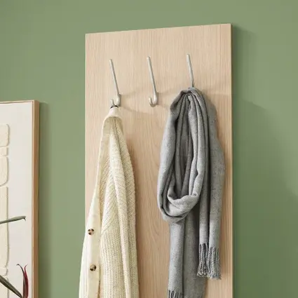 Garderobenpaneel mit Haken an grüner Wand, behängt mit Strickjacke und Schal