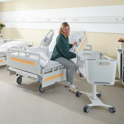 Pacjentka siada na krawędzi łóżka i korzysta z podniesionej barierki bocznej od strony głowy, która pomaga jej wstać i zejść z łóżka.