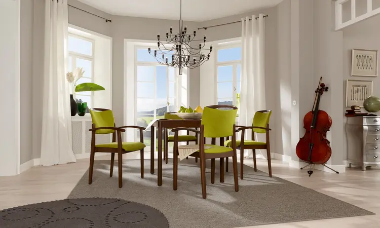 Stapelbarer Stuhl der Serie Fena mit Griffbügel in Holzoptik, stehend an einem Tisch in einem Aufenthaltsraum.