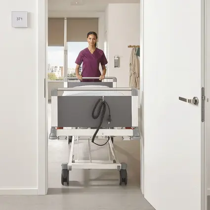 Verzorger duwt smal Evario eenpersoonsbed met een breedte van 89 cm door deur