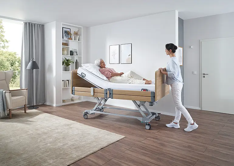 Elvido movo ist elektrisch höhenverstellbar mit Scherenhub und Holzverkleidung für ergonomische Pflege und Tranfer vom Bewohner.