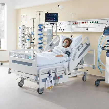 Sala szpitalna z łóżkiem Evario one i sprzętem medycznym, wyposażona w zasilanie i standardowe szyny przesuwne, aby umożliwić optymalną opiekę nad pacjentem.