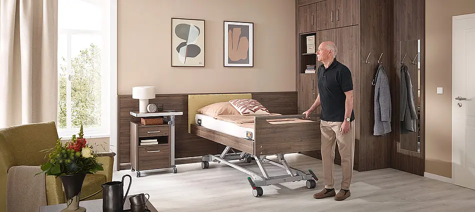 Elvido Pflegebett mit Holzdekor und elektrischer Höhenverstellung. Bietet mit den Fußteil Primus low und dem Holm dem Patienten Sicherheit zum festhalten.