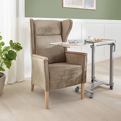 Fotel z wysokim oparciem Luna ze stolikiem nocnym i napojem w nowoczesnym pokoju opieki