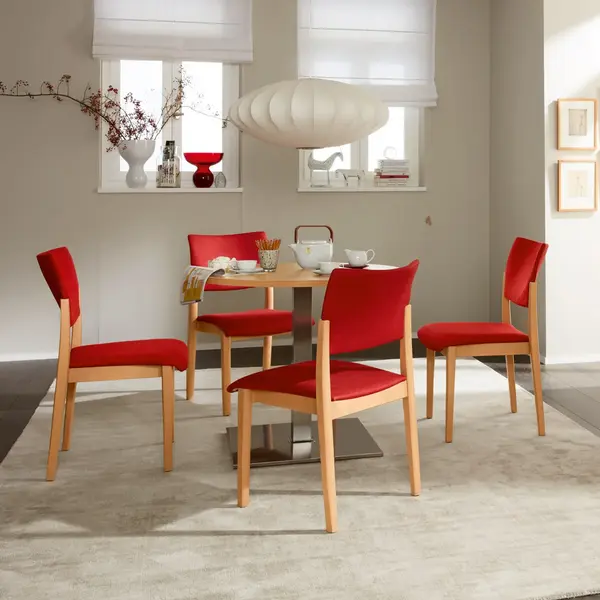 Fena Stuhlserie ohne Griffbuegel mit roten Polster auf Sitzfläche und Rücklehne. Es stehen vier Fena Stühle um einen Tisch, Aufenthaltsraum
